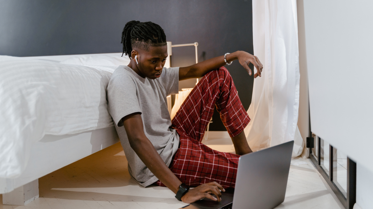 man on bedroom floor looking at laptop